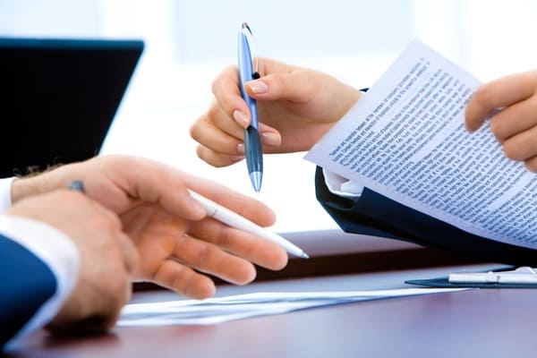 imagen de dos personas trabajando en un documento sobre una mesa. Se ven las manos de un hombre y de una mujer. La mujer sostiene un documento. Representación del asesoramiento a empresas y administraciones