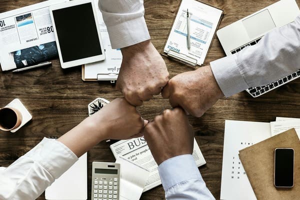 imagen de cuatro puños de personas unidos en sinónimo de cooperación sobre mesa de trabajo con material de oficina